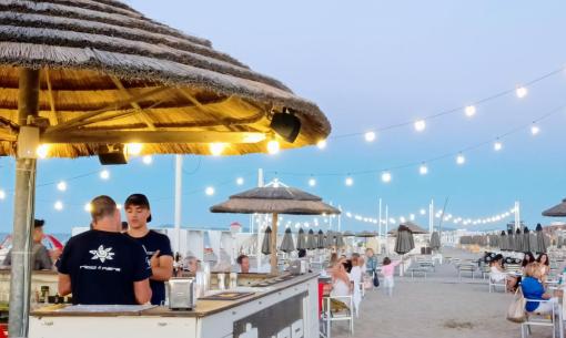 Spiaggia al tramonto con luci e bar all'aperto.