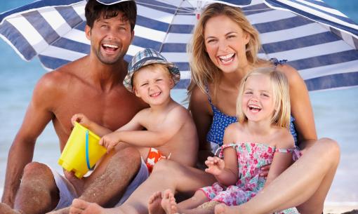 Famiglia felice in spiaggia sotto un ombrellone a righe.