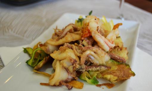 Fritto misto di mare con gamberi e calamari su piatto bianco.