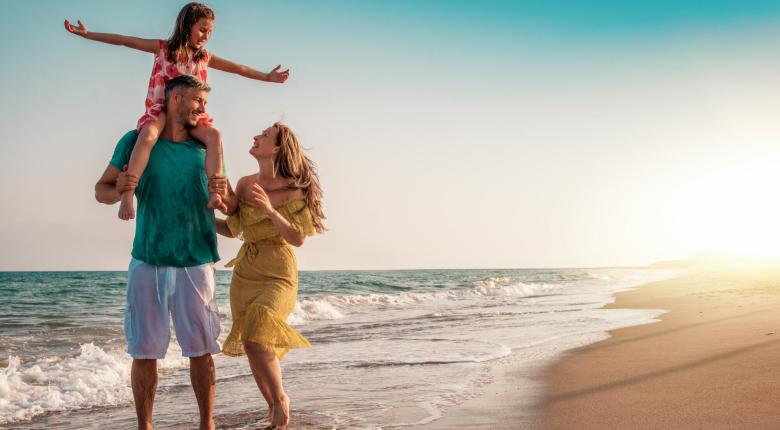 Glückliche Familie spaziert am Strand bei Sonnenuntergang.